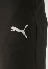 Svarta träningsbyxor med en framträdande vit logotyp av en hoppande katt. Materialet ser mjukt ut med en slät yta. Enkel design utan ytterligare accenter.