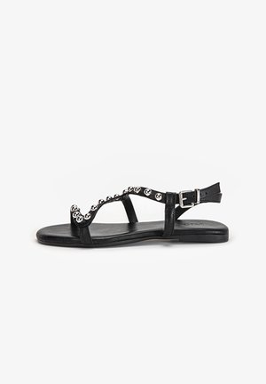 Sort flad sandal med sølvnitter, ankelrem og spænde, med åben tå og minimalistisk design på hvid baggrund.