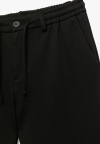 Schwarze Sweathosen mit elastischem Bund, Kordelzug und einem einzigen Knopf, aus einem strukturierten Stoff mit Seitentaschen.