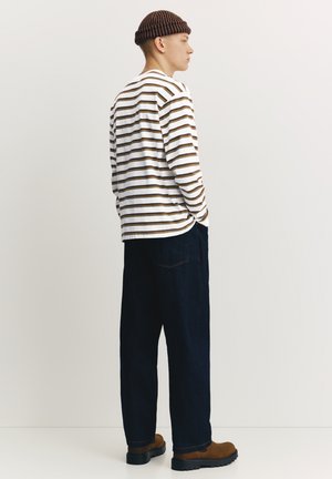 Striped long-sleeve shirt in white, brown, and beige. Loose dark denim pants and brown boots. Wool hat with dark brown and light stripes.