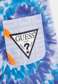 Barvna tie-dye žepna torbica v modri in oranžni barvi s trikotnim črnim oznako, na kateri je napis "GUESS," "WASHED," in simbol vprašaja.
