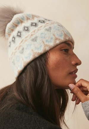 Cappello invernale lavorato a maglia di colore crema con motivi azzurri chiari e marroni, impreziosito da un morbido pompon grigio; realizzato in lana calda e dalla texture avvolgente.