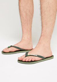 Infradito verdi in gomma con una fascia testurizzata e logo, caratterizzate da una suola a strisce in bianco e giallo. Il design favorisce il comfort e l'abbigliamento casual.