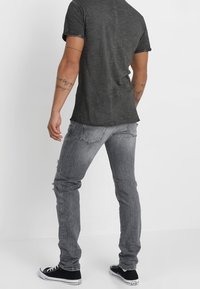 Camiseta gris de cuello redondo, de manga corta, ajuste casual, combinada con jeans gris desgastados y zapatillas negras con acentos blancos.