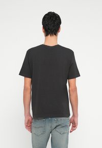 Must lühikeste varrukatega t-särk pehmest puuvillast, millel on ümarselg ja lõdvestunud lõige. Näidatud tagant, sirge ääre ja minimaalsete detailidega.