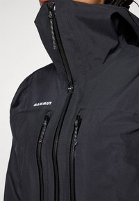 Black waterproof jacket with a high collar, multiple zippered pockets, and branded detail. Smooth texture and fitted design.