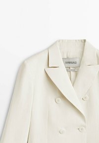 Blazer croisé écru avec larges revers et quatre boutons assortis, étiqueté Massimo Dutti Limited Edition fabriqué au Portugal.