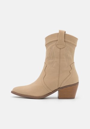 Botte de cowboy beige avec un bout pointu, des coutures décoratives et un talon empilé de 6,5 cm. Fabriquée en matériau souple à texture lisse.