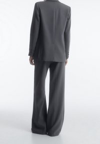 Veste de costume grise cintrée avec un revers en encoche et une fente simple, associée à un pantalon à jambes larges. Tissu doux avec une silhouette épurée.