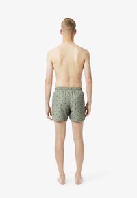 Groene zwemshorts met een patroon, een trekkoord in de taille en een ontspannen pasvorm. Ze hebben kleine groene bladeren tegen een gedempte achtergrond.