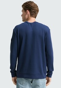 Navyblauer Waffelstrick-Pullover mit langen Ärmeln, gerippten Bündchen und Saum; verfügt über einen schwarzen Akzent am linken Ärmel.