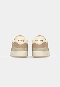 Lacoste sportbačiai su kreminiais ir smėliniais atspalviais, lygios odos viršus, paminkštinta apykaklė ir logotipo detalė kulne.