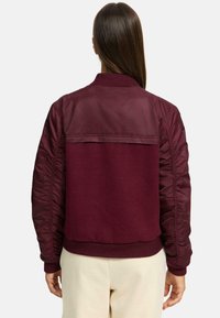 Burgundy bomber jacket with a smooth, shiny upper section and textured wool lower half, featuring ribbed cuffs and a relaxed fit.