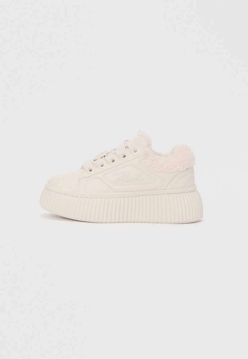Kremfargede sneakers med en teksturert plattformsåle, lisser og en fyldig falsk pelskrage. Har et glatt overmateriale som minner om semsket skinn.