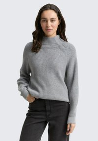 Gray ribbed sweater with a high neck and long sleeves. The fabric appears soft, and the design features a relaxed fit. Paired with black pants.