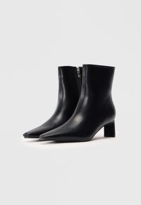 Schwarze Leder-Stiefeletten mit spitz zulaufender Zehe, seitlichem Reißverschluss und einem mittelhohen blockförmigen Absatz. Glatte Textur und elegantes Design.