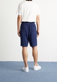 Marina blå bomullsshorts med elastisk midja och en bakficka, kombinerat med en enkel vit t-shirt och vita sneakers.