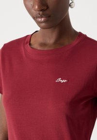 Burgundy short-sleeve T-shirt made of soft cotton, featuring a round neckline and white embroidered logo on the chest.