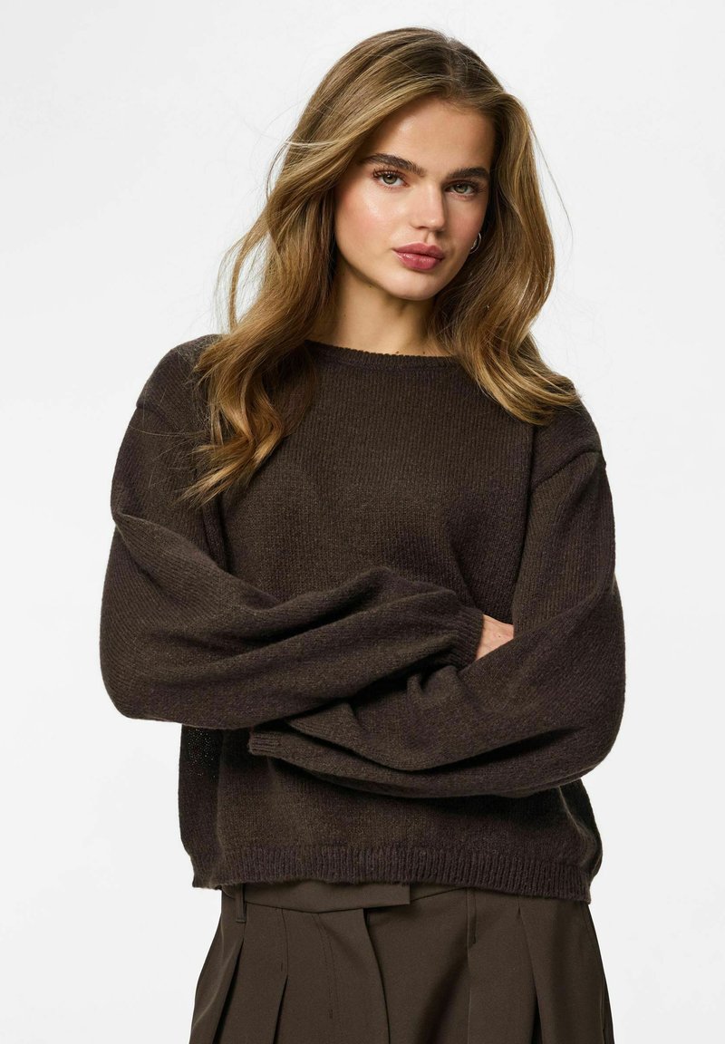 Maglione marrone lavorato a maglia con texture a coste, vestibilità ampia e maniche scese, abbinato a una gonna plissettata coordinata.