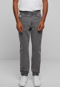 Sive traperice opuštenog kroja s vidljivim šavovima, prednjim džepovima i brandiranim oznakom; uparene s bijelim sportskim tenisicama.