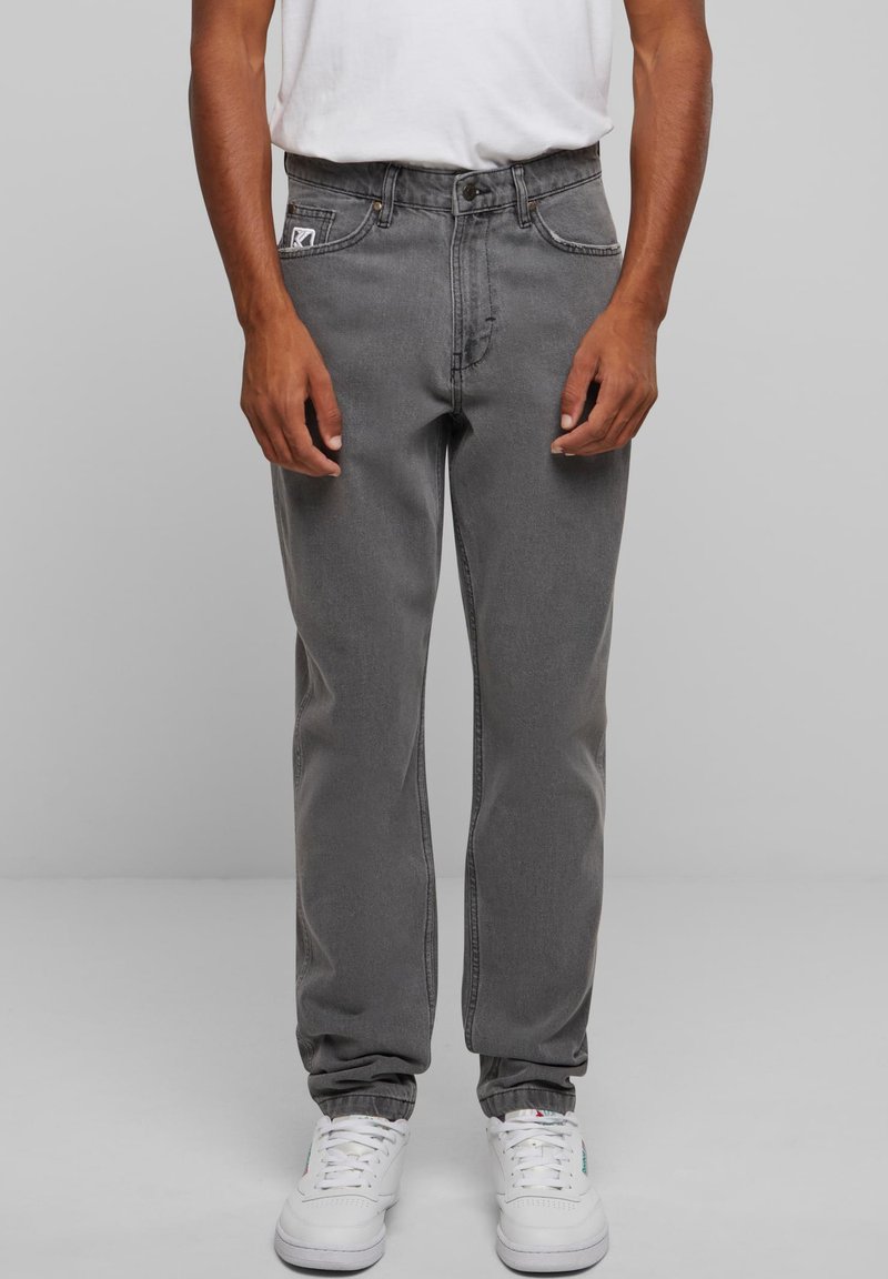 Sive traperice opuštenog kroja s vidljivim šavovima, prednjim džepovima i brandiranim oznakom; uparene s bijelim sportskim tenisicama.