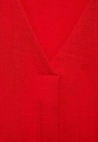 Tissu en lin rouge avec un design à col en V. La texture semble légère et lisse, avec des variations subtiles dans le tissage et la profondeur de la couleur.