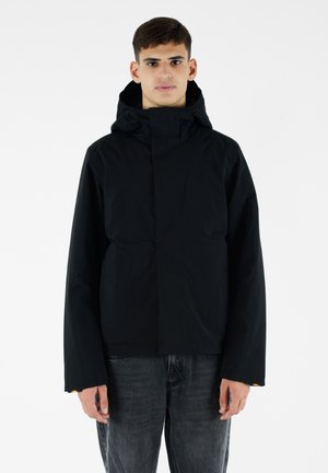 Giacca nera con cappuccio dal design minimalista, caratterizzata da un colletto alto, due tasche frontali e dettagli colorati sulle maniche.