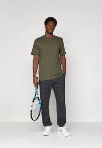 Olivno zelena majica s kratkimi rokavi, kombinirana s temno sivimi trenirkami. Drži teniško lopar; bele športne superge. Enostavna zasnova, minimalno blagovne znamke.