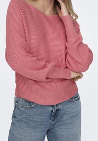 Rosa geripptes Sweatshirt mit weitem Ausschnitt, überschnittenen Schultern und langen Ärmeln. Kombiniert mit hellblauen Jeans.