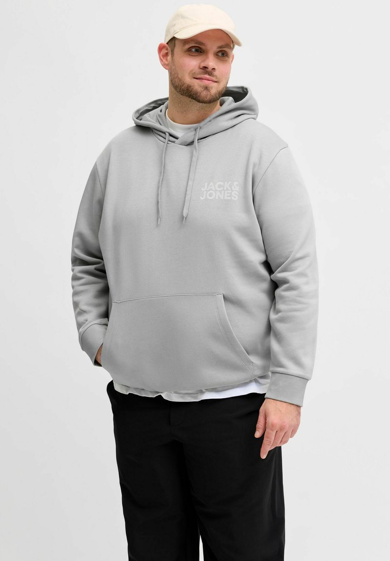 Hellgrauer Hoodie mit Kängurutasche, Kordelzugkapuze und Logo. Kombiniert mit schwarzen Hosen, die eine glatte, legere Stoffstruktur aufweisen.