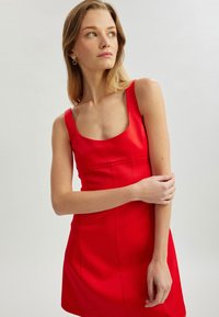 Rotes ärmelloses Kleid mit quadratischem Ausschnitt, taillierter Silhouette und glattem Material. Verfügt über dezente Nahtdetails und ein minimalistisches Design.