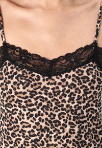 Camisole i leopardmönster med mjukt tyg, tunna axelband och svart spetsdetalj längs halsringningen. Den övergripande designen är figurnära.