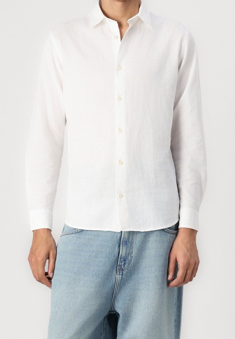 Camicia bianca in lino a maniche lunghe con colletto classico, apertura frontale con bottoni e polsini. Presenta un orlo dritto e un tessuto leggero e strutturato.