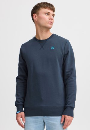 Sudadera azul marino hecha de una mezcla de algodón, con cuello redondo acanalado, mangas largas y un pequeño logo azul en el pecho.