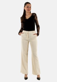 Top nero a maniche lunghe con dettagli in pizzo, abbinato a pantaloni in corduroy crema a gamba larga con vita alta e tasche laterali. Scarpe nere completano il look.