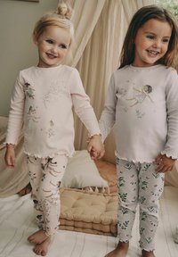 Két gyermek kézen fogva áll, lágy rózsaszín és világosszürke hosszú ujjú felsőket viselnek, melyeken különleges tündér minták láthatók. Feszes leggings-jük virágmintás.