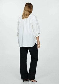 Loose-fit white shirt with gathered back, voluminous sleeves. Paired with black, wide-leg jeans featuring frayed hem and open-toe heels.