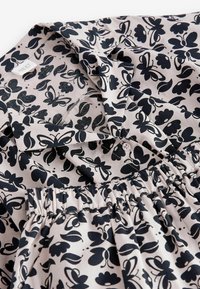 Luftig blus med elastisk midja, i lätt rosa tyg prytt med ett svart blommönster och fjärilar, med en knappad kragedetalj.