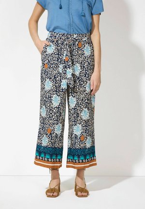 Floral wide-leg pants in navy with turquoise and orange accents. Elastic waist with pockets, patterned fabric, and contrasting hem detail.