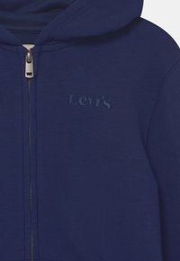 Navy hooded sweatshirt with a silver zipper. Features subtle embroidered Levi's logo. Made of soft fabric with a smooth texture.