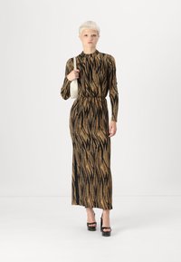 Schwarz-goldenes Langarmkleid mit tailliertem Schnitt und gewelltem Muster. Kombiniert mit schwarzen Plateau-Heels und einer weißen Handtasche.