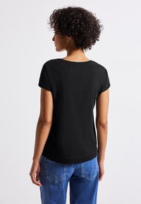 T-shirt noir à manches courtes avec un col rond, fabriqué en tissu doux. Associé à un jean bleu ample, avec des poches visibles.