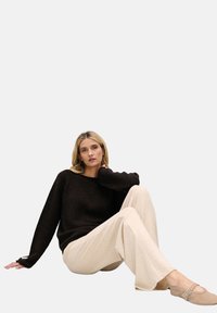 Ciemnobrązowy sweter z dzianiny, beżowe spodnie o szerokich nogawkach i jasne buty. Miękka faktura, luźny krój i minimalistyczny design z delikatnymi liniami.