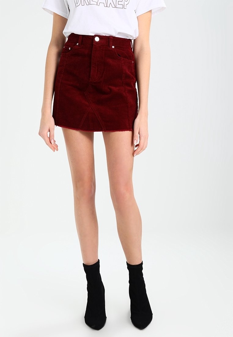 Burgunder färgad kord kjol med framsidor, en svag fransad fåll, tillsammans med en vit t-shirt med tryck och svarta ankelstövlar.