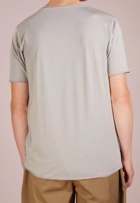 Lichtgrijs t-shirt met korte mouwen, ronde halslijn en gestikte zoom. Heeft een soepele textuur en een langere achterkant. Eenvoudig ontwerp.