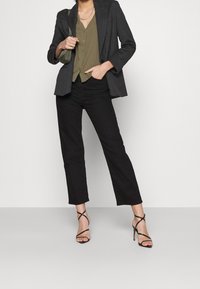 Blaser à rayures noires, chemise boutonnée vert olive, pantalon noir et sandales à talons. Caractéristiques : coupe ajustée, col et coupe à la cheville.