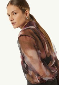 Sheer blouse with abstract maroon and brown patterns, featuring a high collar and long sleeves. Fabric appears lightweight and flowing.