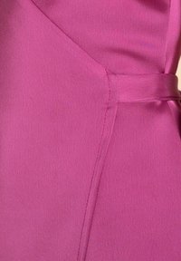 Vestido fucsia con una tela suave y texturizada, con una costura lateral y un cinturón de tela para un detalle adicional. Silueta clásica con un diseño estructurado.