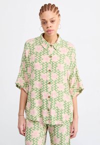 Korte mouwenshirt in lichtgroen, met golvende patronen en roze bloemen. Heeft een knoopsluiting aan de voorkant en een kraag, gemaakt van lichtgewicht stof.