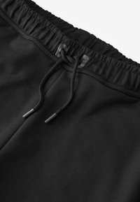 Zwarte joggingbroek met een elastische tailleband, voorzien van een vetersluiting en plastic uiteinden. Textiel met een gestructureerde stof en een gladde afwerking.